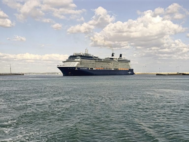 Elegant cruise ship navigates calm waters in a Spanish harbor under a partly cloudy sky.