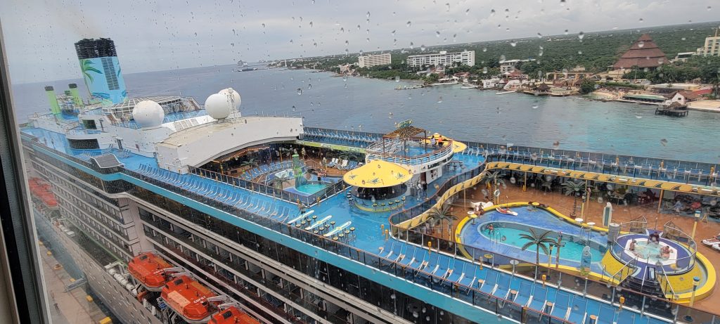 Looking down at the colorful pool deck and tropical themed funnel of Margaritaville at Sea docked in Cozumel, Mexico.