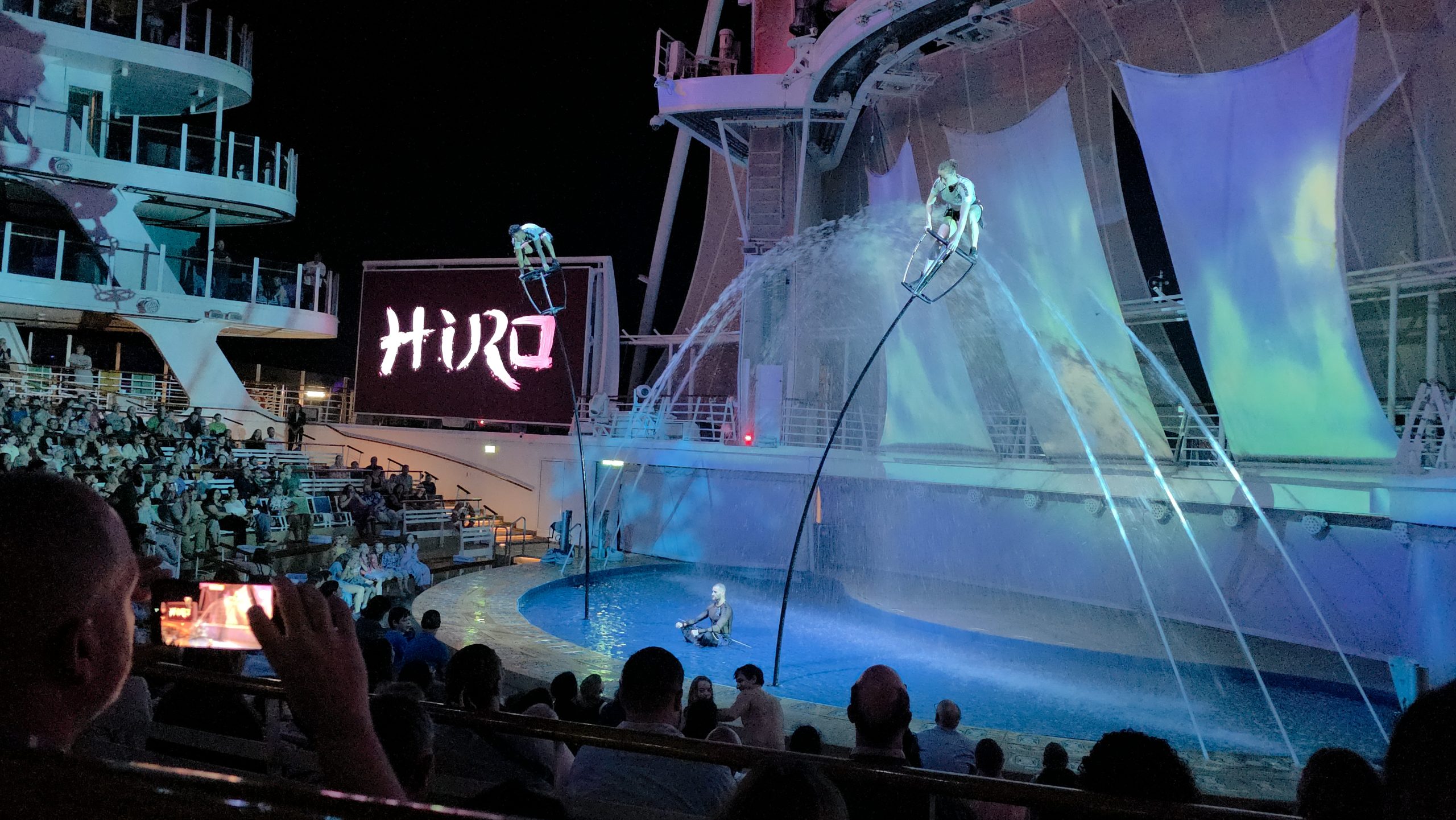 A live evening performance of the Hiro aqua show featuring high-diving acrobats at the outdoor AquaTheater onboard Symphony of the Seas.