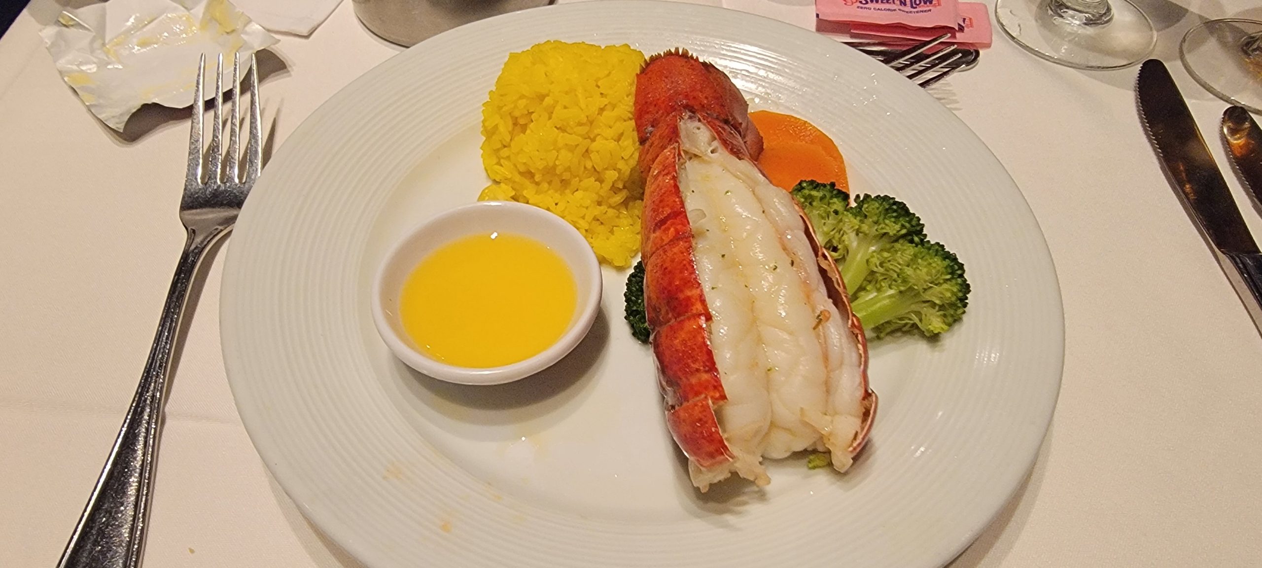 A close-up of a lobster night dinner plate on Harmony of the Seas featuring a lobster tail, yellow rice, a side of melted butter, and broccoli.