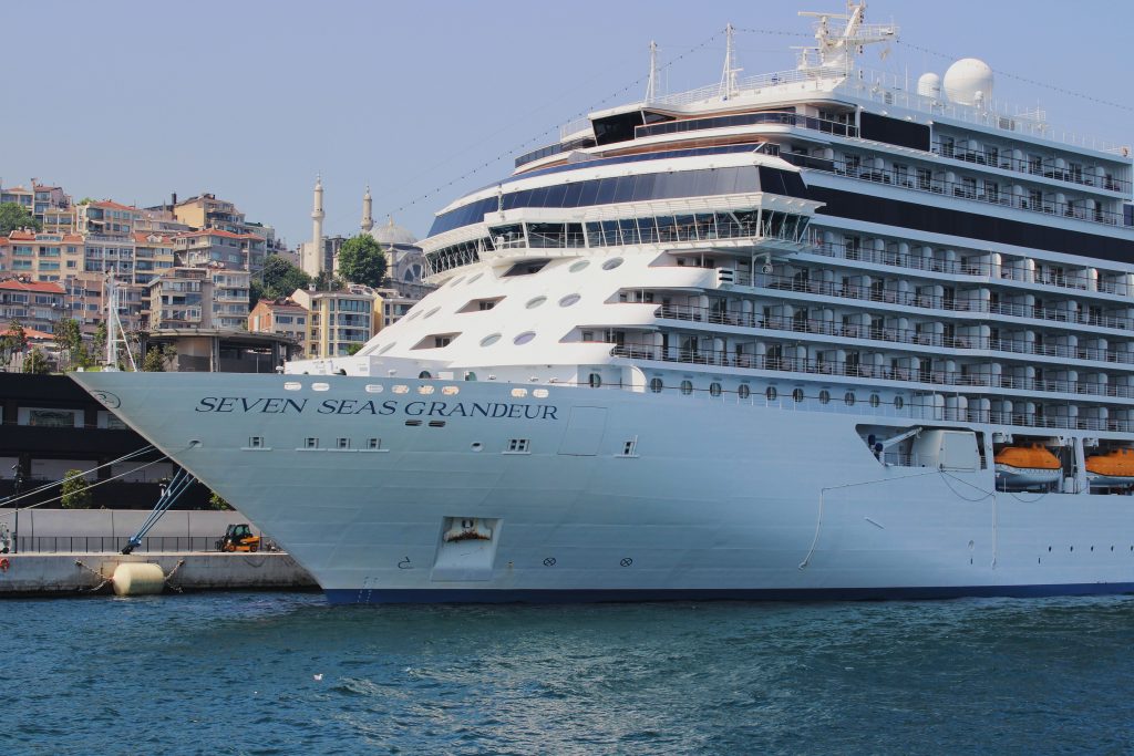 A close-up side profile of the pristine white ultra-luxury ship Seven Seas Grandeur docked in the blue waters of Istanbul, Turkey.