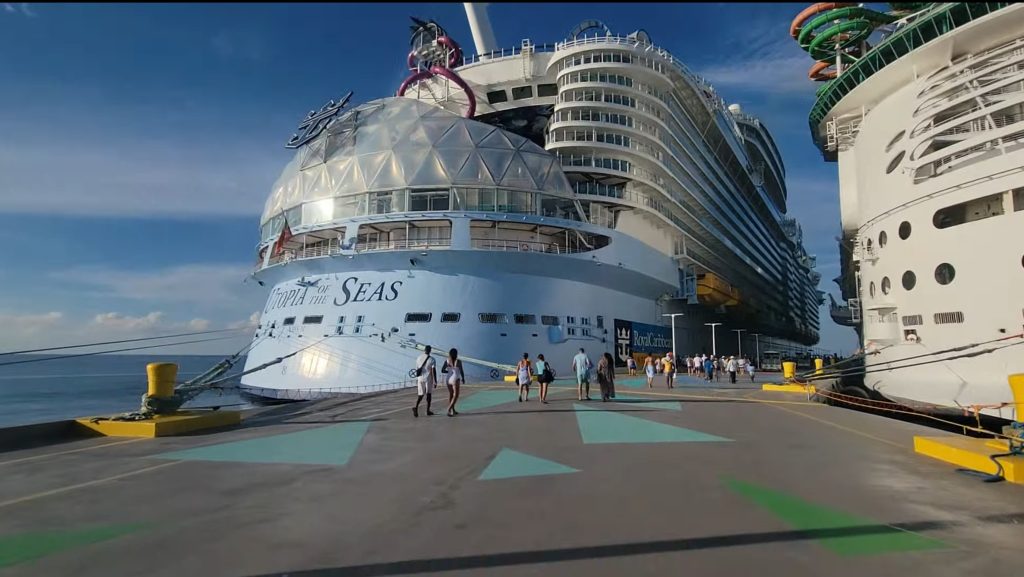 A crisp, close-up view of the aft and glass Solarium dome of Royal Caribbean's Oasis-class Utopia of the Seas docked at a pier, with the ship's name clearly visible on the stern.